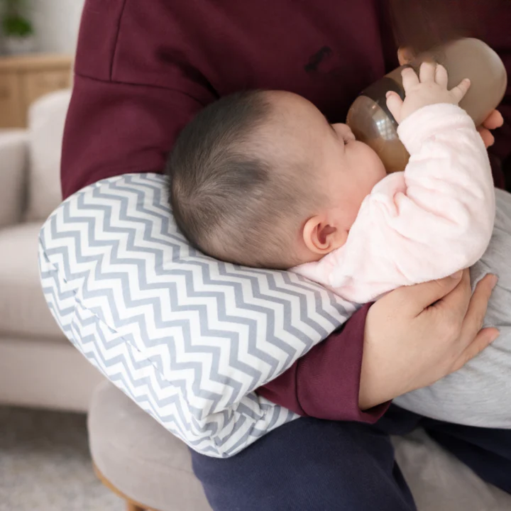 Baby bottle feeding while supported by gray chevron Arm-Stillkissen pillow