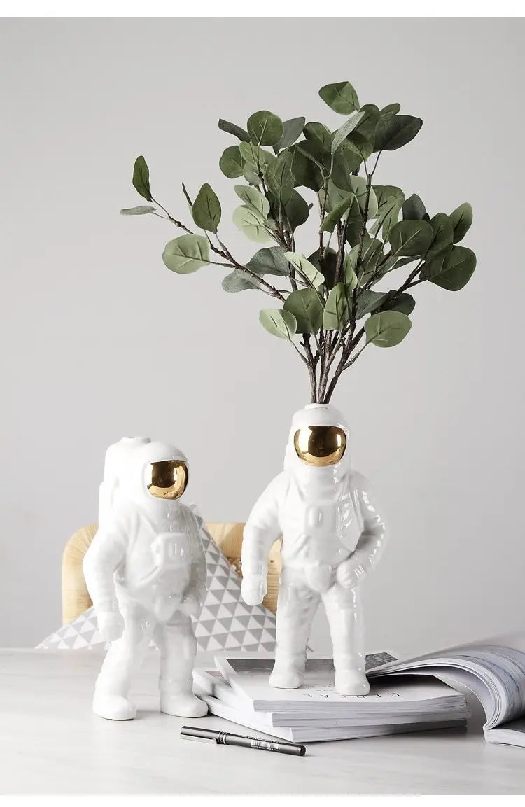 Two white astronauten-figur planters holding green eucalyptus branches on desk