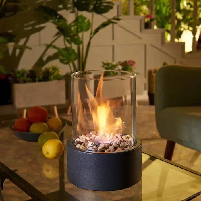Tragbare Tischfeuer-Laterne with black base on glass table with fruit